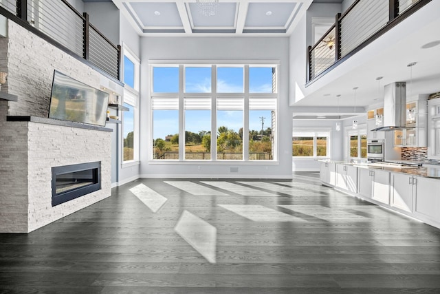 unfurnished living room with dark hardwood / wood-style flooring, a stone fireplace, plenty of natural light, and coffered ceiling