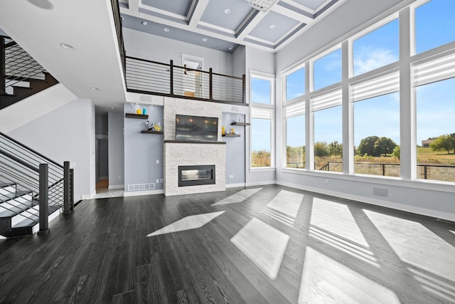 unfurnished living room with coffered ceiling, beamed ceiling, a towering ceiling, wood-type flooring, and a fireplace