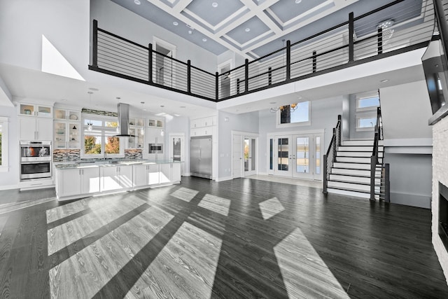 living room with dark wood-type flooring, coffered ceiling, a towering ceiling, a chandelier, and a fireplace