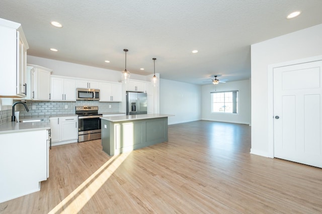 kitchen featuring pendant lighting, white cabinets, sink, a kitchen island, and stainless steel appliances