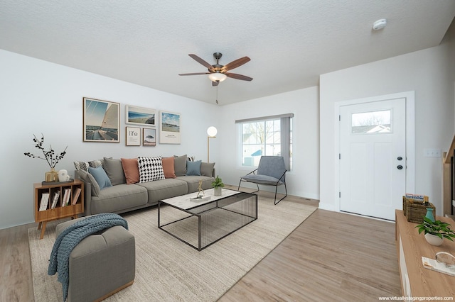 living room featuring ceiling fan, light hardwood / wood-style floors, and a textured ceiling