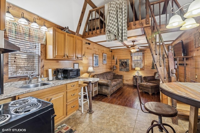 kitchen with ceiling fan, sink, light stone counters, range with electric stovetop, and wood walls