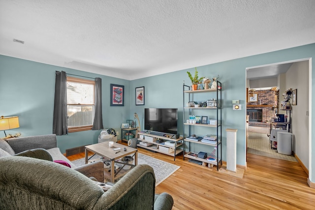 living room featuring hardwood / wood-style flooring, a brick fireplace, and a textured ceiling