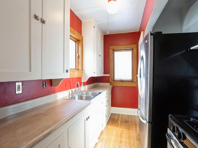 kitchen with white cabinets, appliances with stainless steel finishes, light hardwood / wood-style floors, and sink