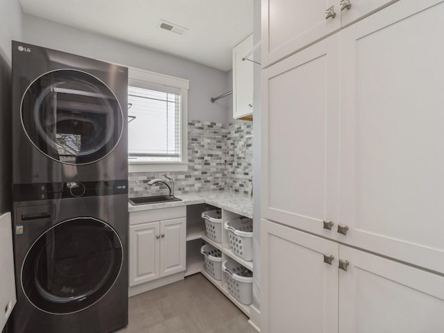 laundry area featuring stacked washer and dryer, cabinets, and sink