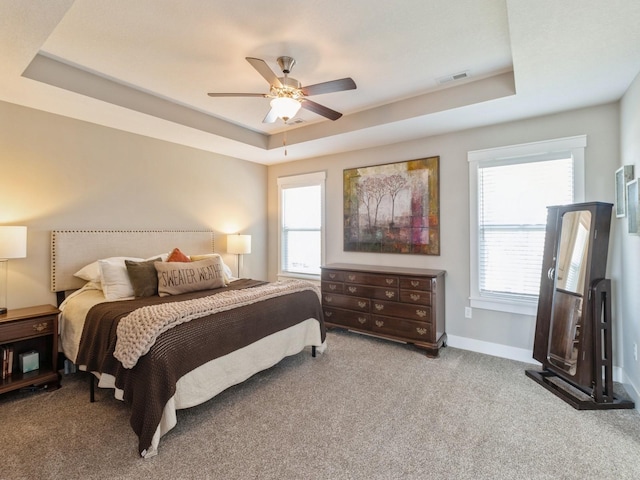 bedroom featuring light carpet, a tray ceiling, and ceiling fan