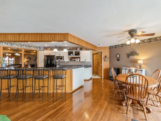 kitchen featuring white cabinetry, ceiling fan, wood walls, light hardwood / wood-style floors, and black refrigerator