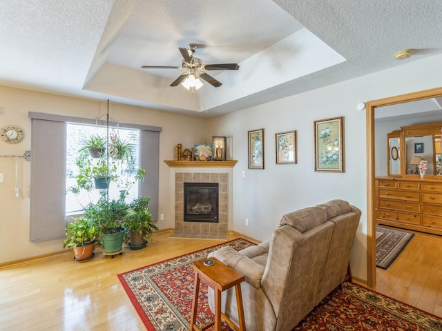 living room featuring ceiling fan, a raised ceiling, wood-type flooring, a textured ceiling, and a tiled fireplace