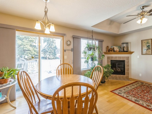 dining area featuring light hardwood / wood-style flooring, a textured ceiling, a tray ceiling, a fireplace, and ceiling fan with notable chandelier