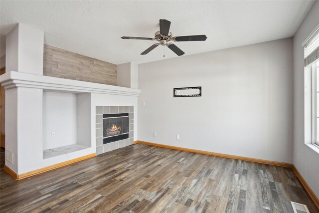 unfurnished living room featuring a tiled fireplace, ceiling fan, dark wood-type flooring, and a textured ceiling