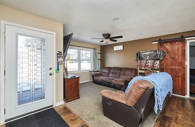 living room with a barn door, ceiling fan, dark hardwood / wood-style floors, and a textured ceiling