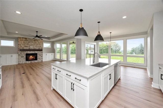 kitchen with sink, a stone fireplace, light stone counters, a center island with sink, and white cabinets