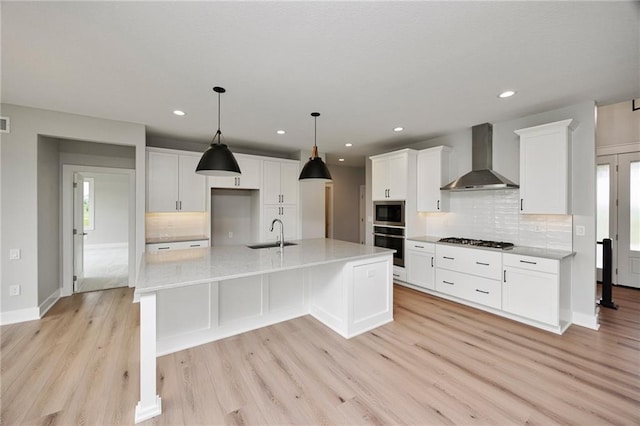 kitchen with white cabinets, stainless steel appliances, an island with sink, and wall chimney range hood