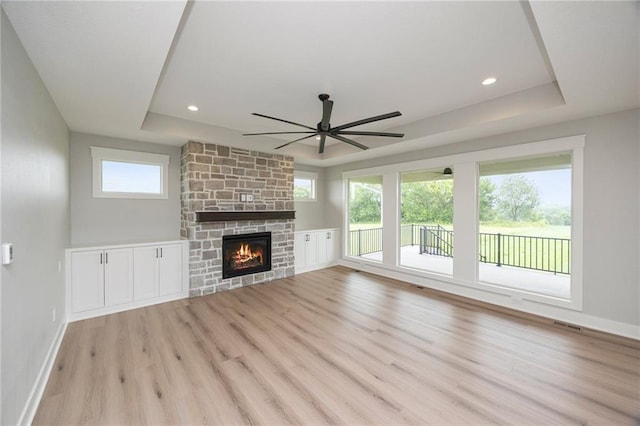 unfurnished living room featuring a healthy amount of sunlight, light hardwood / wood-style flooring, a fireplace, and a tray ceiling