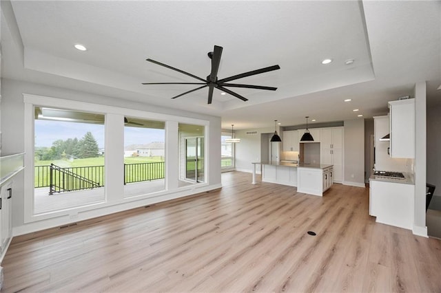 unfurnished living room with a tray ceiling, light hardwood / wood-style floors, and ceiling fan