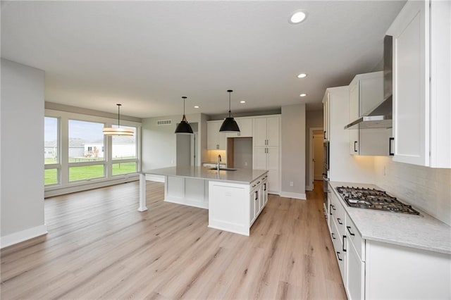 kitchen with sink, hanging light fixtures, stainless steel appliances, a kitchen island with sink, and white cabinets