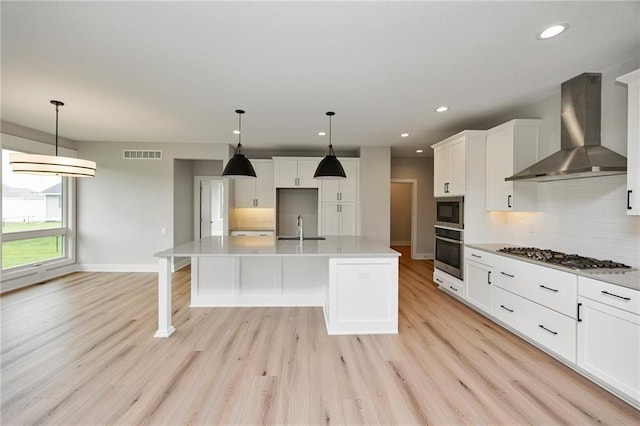 kitchen featuring decorative light fixtures, a center island with sink, wall chimney exhaust hood, and appliances with stainless steel finishes