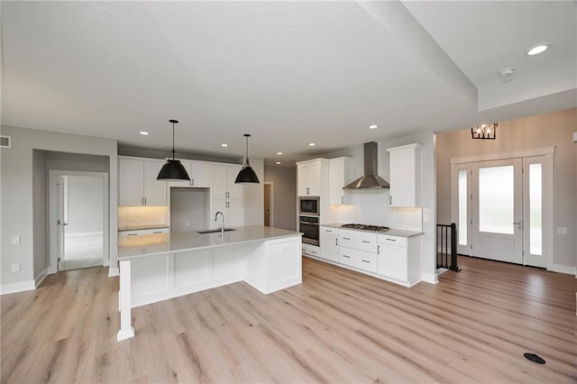 kitchen featuring stainless steel appliances, white cabinetry, a kitchen island with sink, and wall chimney range hood