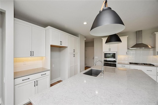 kitchen with sink, appliances with stainless steel finishes, white cabinetry, light stone counters, and wall chimney exhaust hood