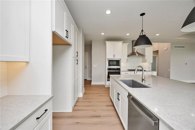 kitchen with pendant lighting, sink, appliances with stainless steel finishes, light stone counters, and wall chimney exhaust hood