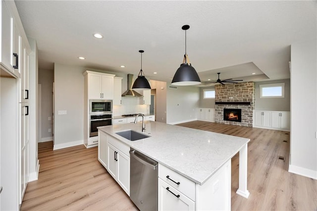 kitchen with appliances with stainless steel finishes, white cabinetry, sink, a center island with sink, and wall chimney range hood