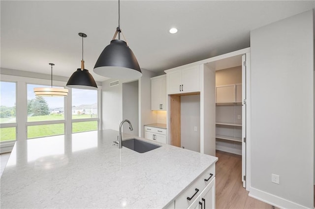 kitchen with white cabinetry, sink, light stone counters, and decorative light fixtures