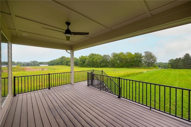 wooden terrace featuring ceiling fan, a lawn, and a rural view