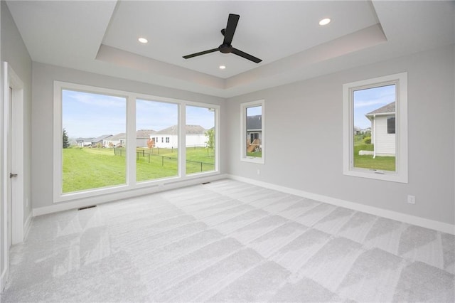 spare room featuring ceiling fan, light colored carpet, and a tray ceiling