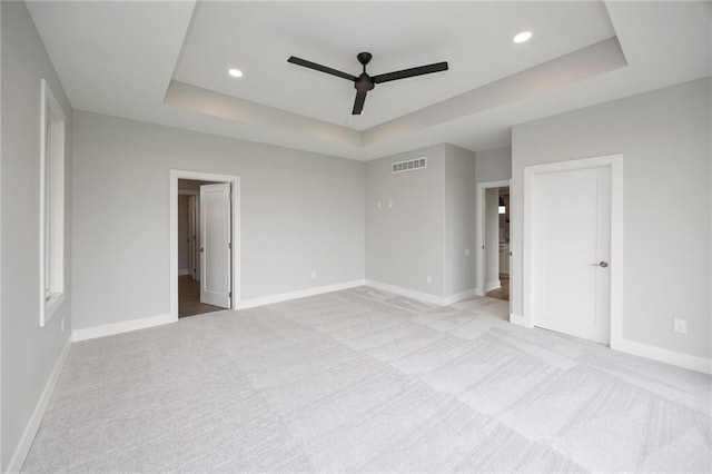 unfurnished bedroom with a raised ceiling, light carpet, and ceiling fan