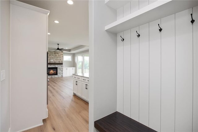 mudroom featuring ceiling fan, a fireplace, and light wood-type flooring