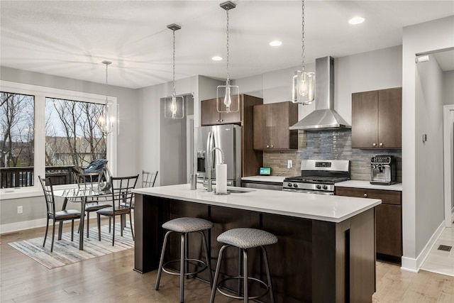 kitchen featuring pendant lighting, wall chimney exhaust hood, appliances with stainless steel finishes, tasteful backsplash, and dark brown cabinets