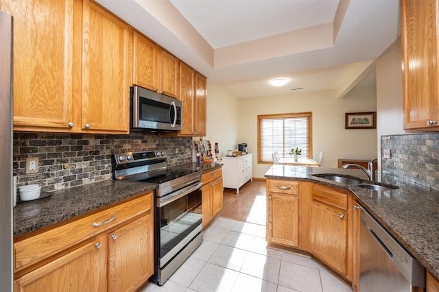 kitchen with dark stone countertops, sink, stainless steel appliances, and light tile patterned flooring