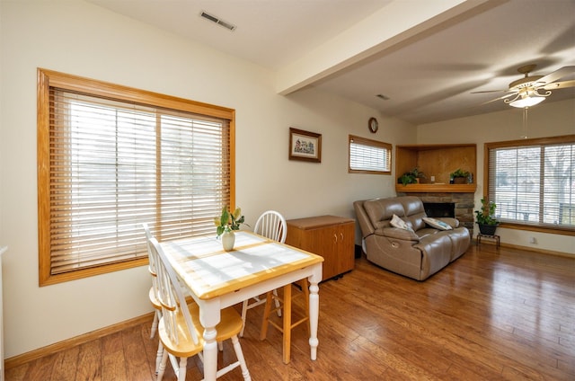 dining room with hardwood / wood-style floors, a wealth of natural light, a fireplace, and ceiling fan