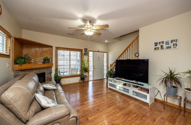 living room with ceiling fan, a stone fireplace, and hardwood / wood-style floors