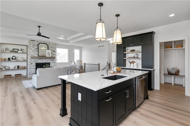 kitchen with pendant lighting, a fireplace, dishwasher, sink, and a center island with sink