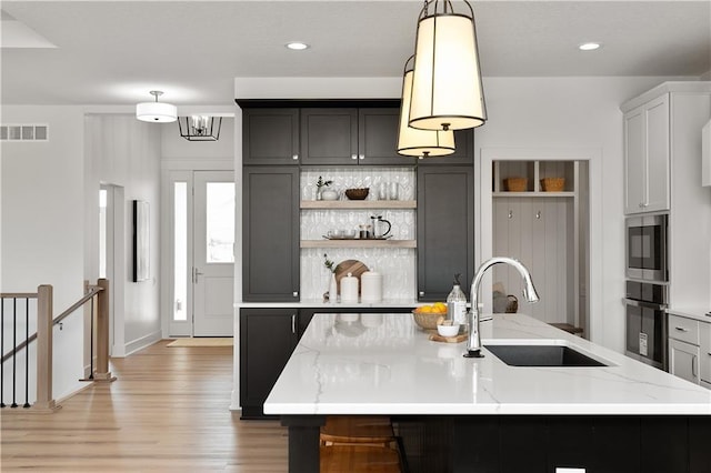 kitchen with appliances with stainless steel finishes, pendant lighting, sink, backsplash, and a center island with sink