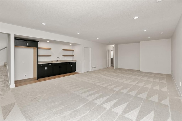 unfurnished living room featuring indoor wet bar, light carpet, and a textured ceiling