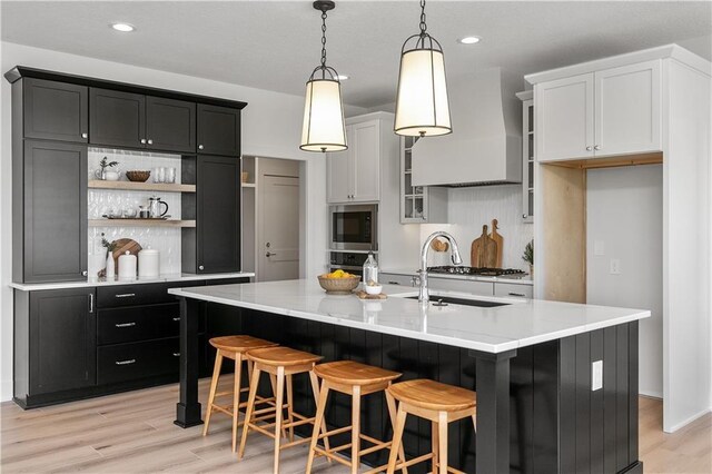 kitchen featuring a center island with sink, white cabinetry, built in microwave, and custom exhaust hood