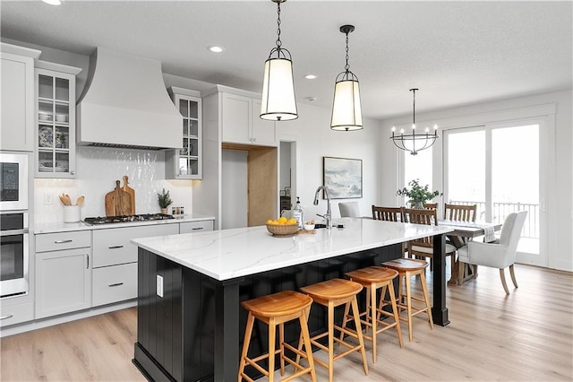 kitchen with white cabinetry, an island with sink, appliances with stainless steel finishes, and premium range hood