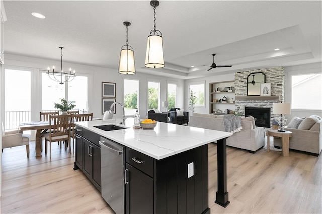 kitchen with sink, stainless steel dishwasher, a tray ceiling, an island with sink, and pendant lighting