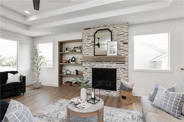 living room with a tray ceiling, hardwood / wood-style flooring, a fireplace, and built in shelves