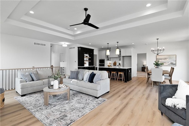 living room featuring a tray ceiling, ceiling fan with notable chandelier, and light hardwood / wood-style floors