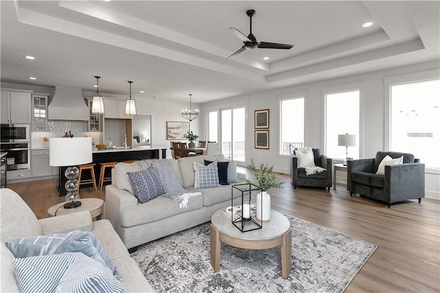 living room featuring a raised ceiling, ceiling fan with notable chandelier, and light hardwood / wood-style flooring