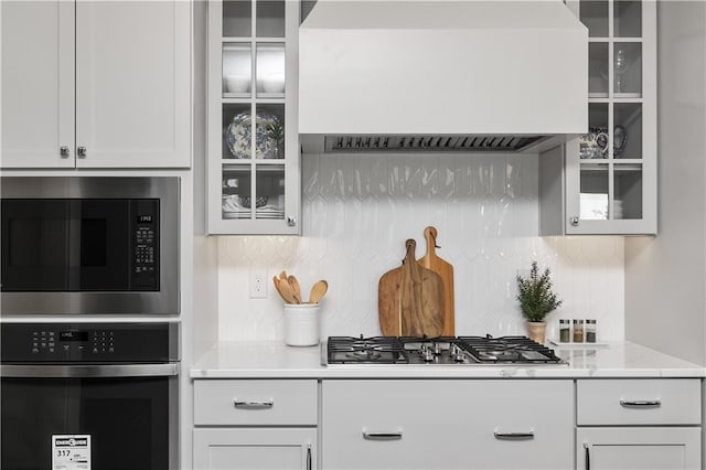 kitchen featuring stainless steel appliances, white cabinetry, custom range hood, and tasteful backsplash