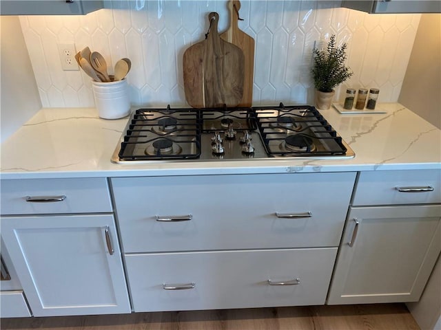 interior details with light stone counters, white cabinetry, gas cooktop, dark hardwood / wood-style floors, and decorative backsplash