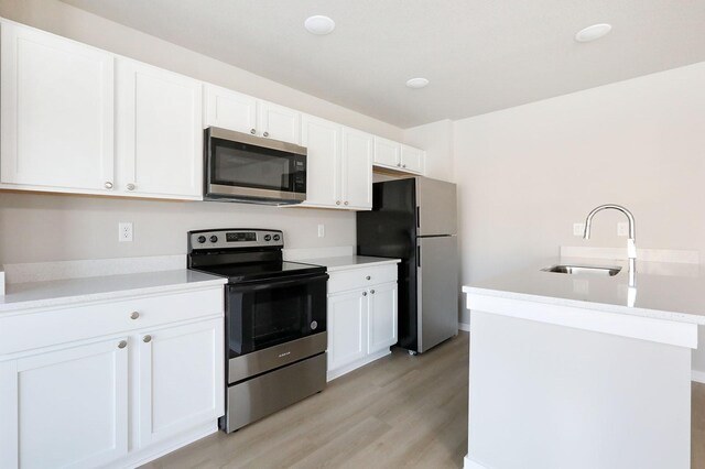 kitchen with appliances with stainless steel finishes, light hardwood / wood-style flooring, white cabinetry, and sink