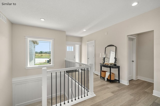 hallway with a textured ceiling and light hardwood / wood-style flooring