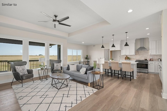 living room with light hardwood / wood-style floors, a raised ceiling, plenty of natural light, and ceiling fan