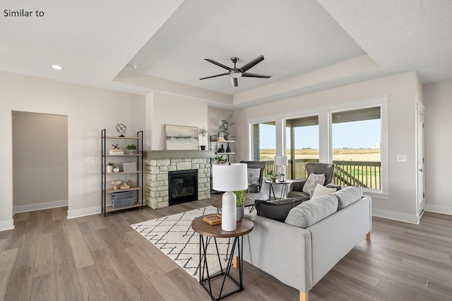 living room with a raised ceiling, ceiling fan, a fireplace, and hardwood / wood-style flooring