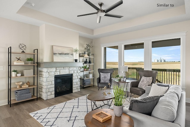 living room with a raised ceiling, dark hardwood / wood-style flooring, ceiling fan, and a fireplace